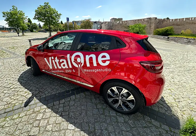 Roter Seat Arona, beklebt mit weißem Logo und Text des Massagestudios Vital One, vor einer Burg.